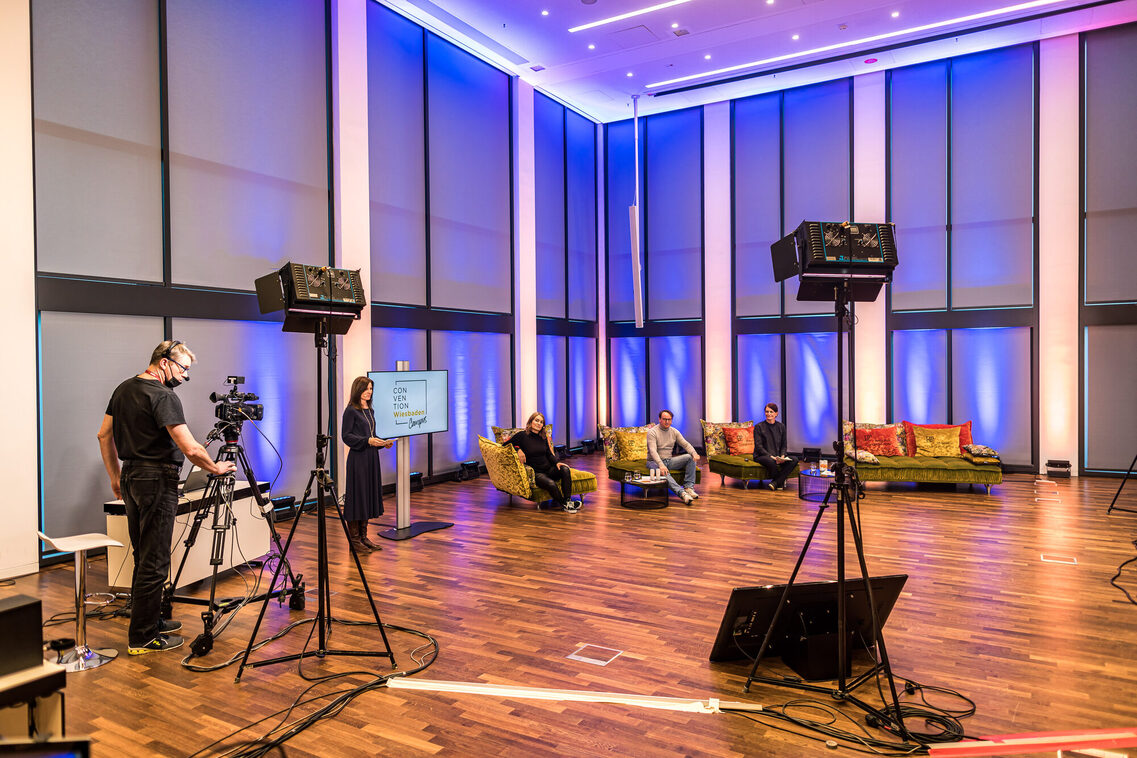 Eine Moderatorin, drei Referenten und ein technischer Mitarbeiter bereiten sich im Studio für Live-Stream vor