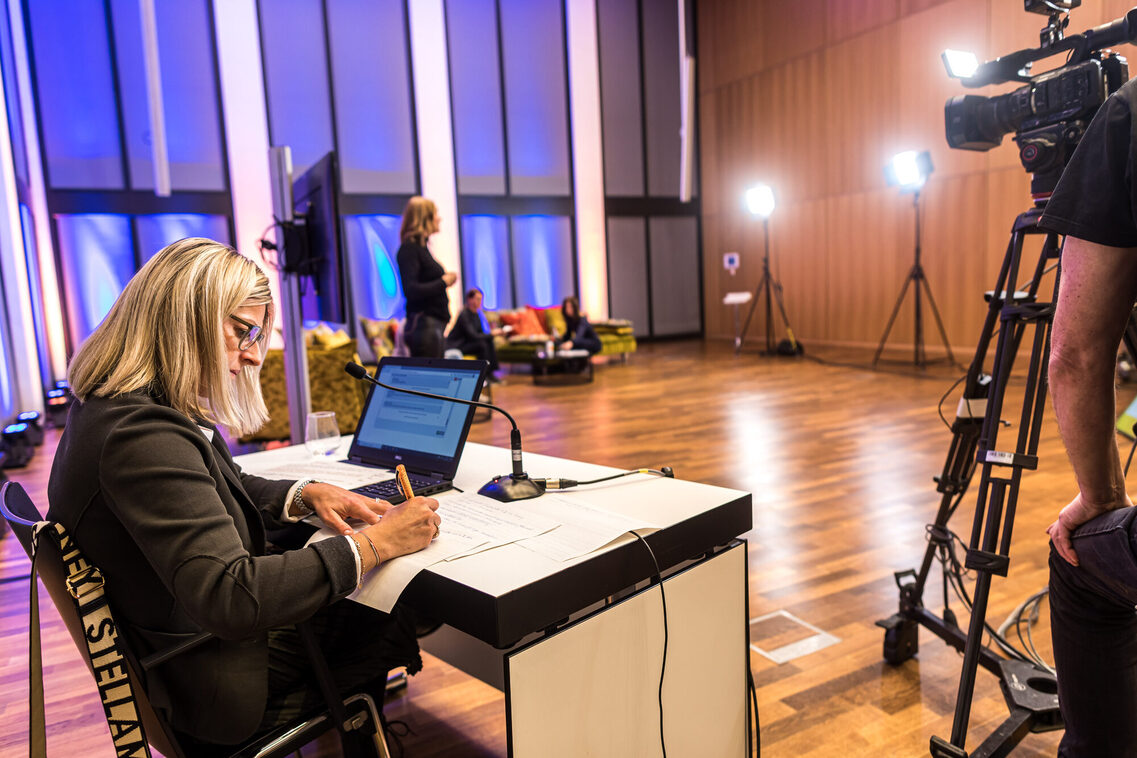 Eine Mitarbeiterin notiert Fragen der Teilnehmer während des Live-Streams im Studio