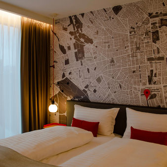 Doppelbett mit zwei großen weißen und zwei kleinen roten Kissen. An der Wand ist die Karte von Wiesbaden zu sehen.