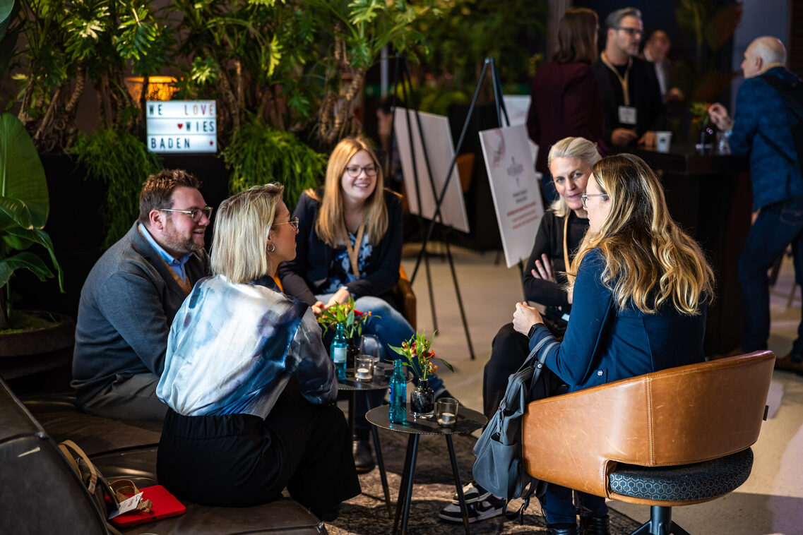 Menschen sitzen in der Messehalle und unterhalten sich