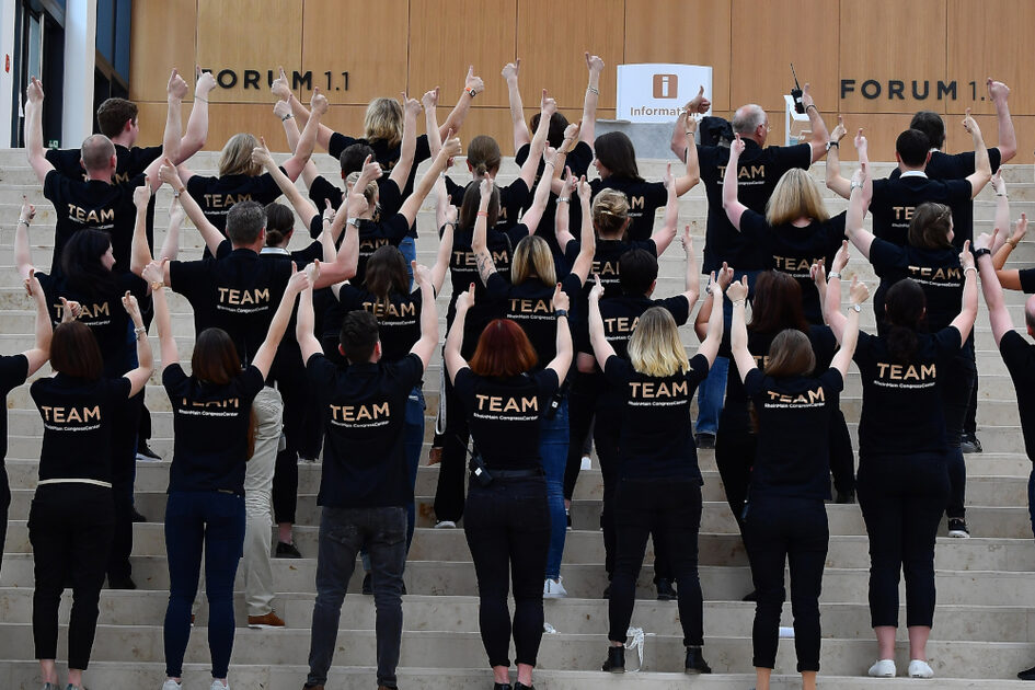 Gruppenfoto des Teams von hinten. Personen stehen auf Stufen und strecken die Fäuste gen Himmel.
